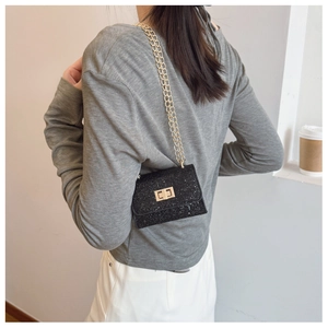 Detail of mini black glitter bag with gold rotating lock and chain strap on shoulder