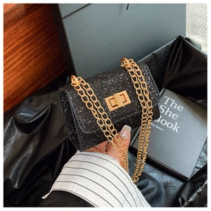 Detail of black glitter crossbody bag featuring gold chain straps and a metallic turn-lock