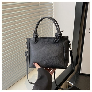 Detail of black lychee grain leather handbag with embossed fashion logo and knotted handles