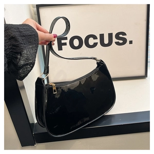 Close-up of black patent leather baguette bag with premium gold metal zipper details