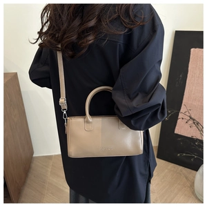 Modèle portant un sac bandoulière beige rectangulaire avec lettrage embossé
