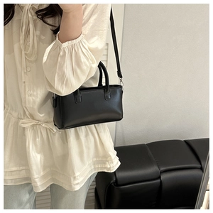 Detail of a black minimalist rectangular handbag featuring matte leather and a metal clasp