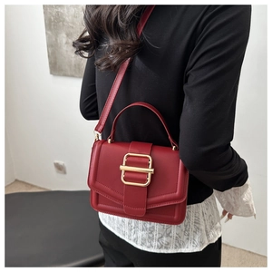 Detailed view of trendy red leather square bag with gold buckle on a model's shoulder