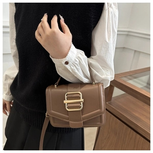 Detail view of brown matte leather crossbody bag with a wide gold buckle on the front