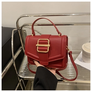 Detail of red leather square handbag with gold buckle on a minimalist display shelf
