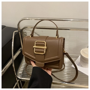 Detailed close-up of brown mocha leather crossbody bag with bold gold metal buckle hardware