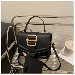 Detail view of black matte leather handbag with gold rectangular buckle on a display stand