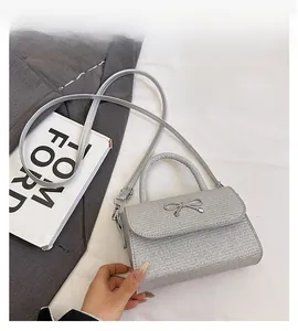 Detailed view of a silver glitter crossbody bag with a metallic bow and top handle