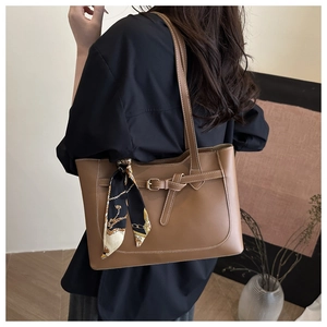Close-up of brown tote bag with decorative buckle and printed silk scarf on handle