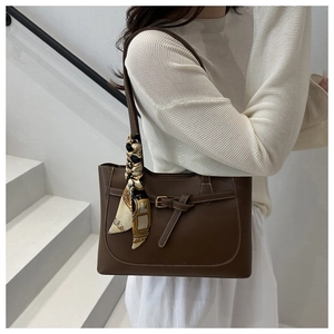 Detail of dark brown tote bag featuring a decorative silk scarf and metal hardware