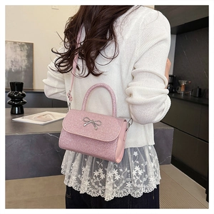 Sac bandoulière pailleté rose avec nœud argenté porté par un mannequin en intérieur