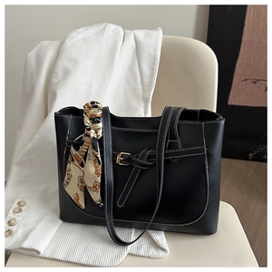 Close-up of black tote bag with white contrast stitching and printed silk scarf on handle