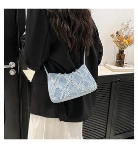 Detail of light blue denim shoulder bag with fringe texture and cross-pattern finish
