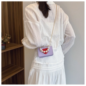 Detail of purple crossbody bag with red heart, pearl handle, and metal chain strap