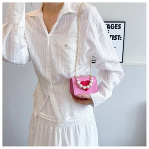 Pink heart crossbody bag with pearl handle and gold chain shown on a model