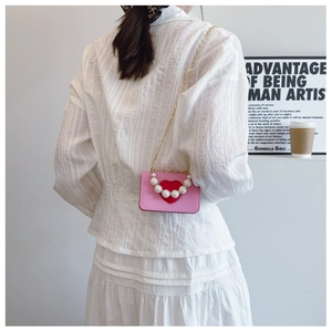 Detail of mini pink heart shoulder bag with pearl handle and golden chain on a model