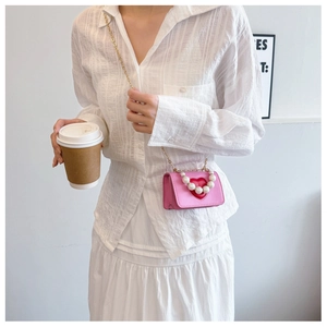 Detail of mini pink crossbody bag with a red heart and pearl accents on gold chain strap