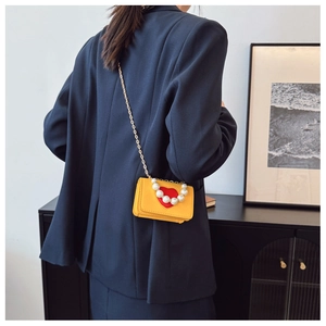 Detail of yellow mini crossbody bag with red heart, pearl handle and gold chain strap