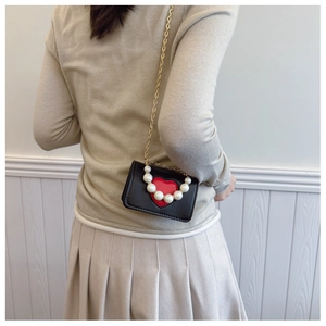 Detail view of mini black crossbody bag with red heart and decorative pearl handle