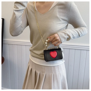 Mini black leather crossbody bag with red heart detail and pearl handle on a model