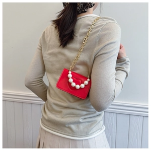 Detail of red heart-embossed bag with pearl handle and golden chain strap