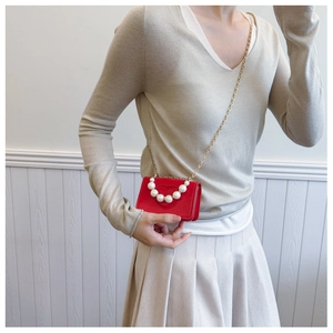 Detail of red heart-embossed mini bag with pearl handle and golden chain strap