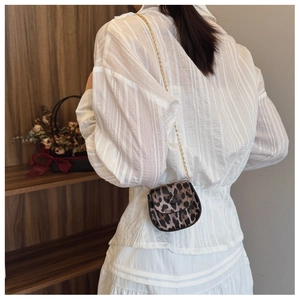 Close-up of a mini leopard print saddle bag with a gold chain strap worn by a model