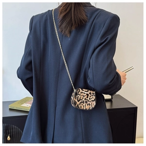 Close-up of mini leopard print saddle bag with gold chain strap on dark suit background