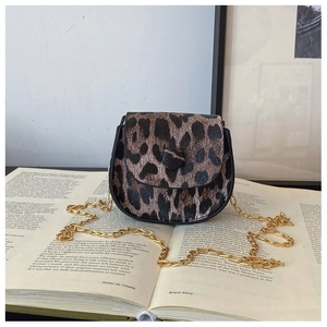 Detail of leopard print crossbody bag with gold chain strap on an open book background