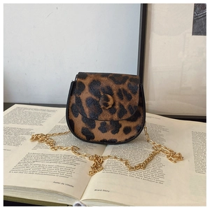 Close-up of leopard print saddle bag with gold chain strap on an aesthetic book background