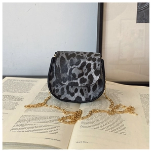 Detailed view of leopard print saddle bag with gold chain strap on an open book