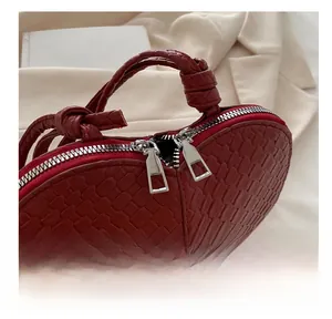 Detail view of red heart-shaped woven bag showing dual metal zippers and knit texture
