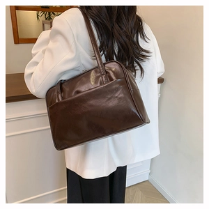 Deep brown glossy leather underarm bag worn by a model in a minimal indoor setting