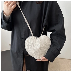 Detailed view of white heart-shaped crossbody bag with crocodile embossed texture on a model