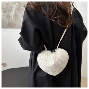 Detail of white heart-shaped crossbody bag with crocodile texture on a black coat