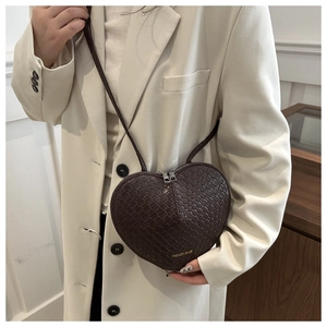 Detail of a dark brown heart-shaped crossbody bag with woven texture on a model
