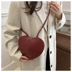 Detail of red heart-shaped shoulder bag with crocodile texture on white blazer