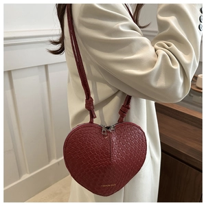 Detail of burgundy heart-shaped crossbody bag with woven texture worn by a model