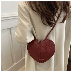 Detail of red heart-shaped crossbody bag with woven texture worn over white blazer