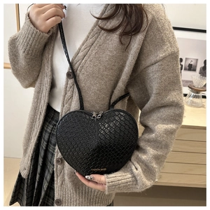 Detail of a black heart-shaped crossbody bag with woven texture and gold fashion logo