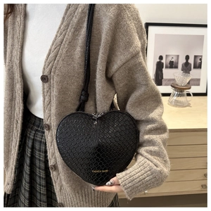 Detailed view of black heart-shaped woven bag with gold logo on a model in home setting