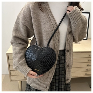 Model wearing black heart-shaped crossbody bag with crocodile texture and silver zippers