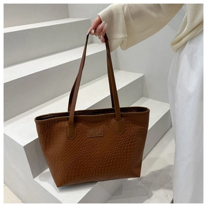 Dettaglio di una borsa tote marrone con trama intrecciata e spalline su gradini bianchi