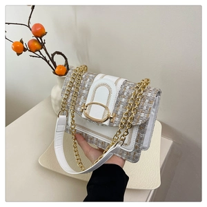 Detail of tweed crossbody bag with golden oval buckle and chain strap on decorative tray