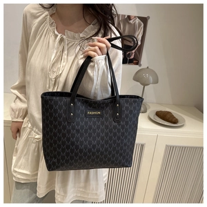 Detail of black tote bag featuring grey M patterns and gold-tone FASHION metal plaque