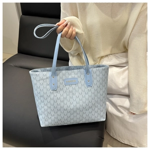 Close-up of light blue tote bag featuring embossed M pattern and gold Fashion plaque