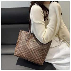 Detail of a brown monogram tote bag with gold logo plate and dual shoulder straps