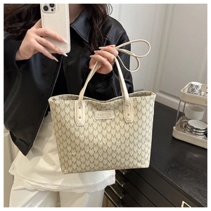 Detail of beige tote bag with M-pattern monogram and fashion brand label being held