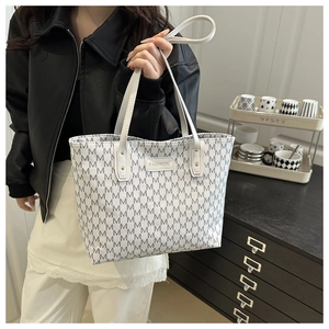 Close-up of white tote bag featuring grey M-pattern print and luxury metal logo detail