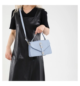 Close-up of light blue flap square bag with gold U-shaped buckle and leather dress